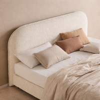 Stoppad säng med sänggavel i bouclétyg och mjuka naturtoner i ett harmoniskt sovrum.